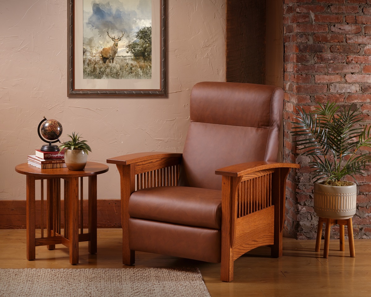 Cozy reading nook featuring a Mission-style recliner in rich brown leather, paired with an oak side table. The setting is enhanced by a rustic brick wall, a textured beige rug, and decorative elements including a globe, books, and potted plants beside an oil painting of a landscape.